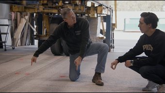 Professor John Haddock and graduate student Oscar Moncada examine a slab of concrete pavement they tested to handle heavy truckloads with wireless power=transfer technology installed below the surface. The machine behind them is designed to imitate those loads by repeatedly passing half a loaded semi-truck axle across the concrete slab. Photo By Consensus Digital Media