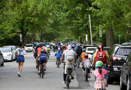 View from behind of dozens of children and some adults traveling along street in bike bus
