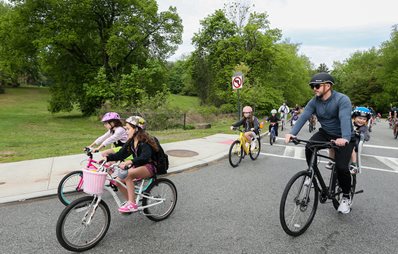 Adult on bike chaperones bike bus of children on bikes in street